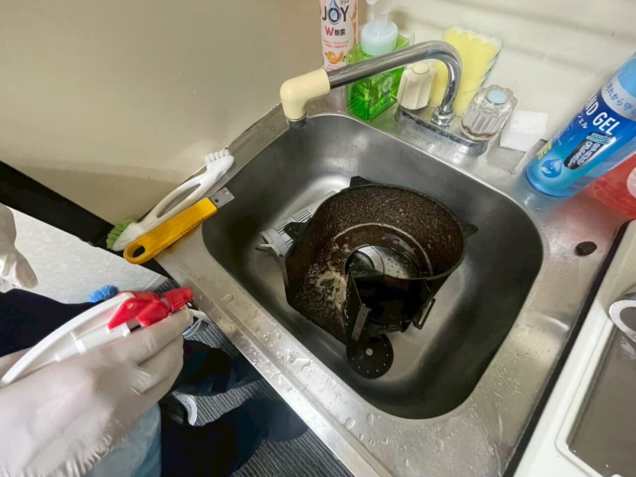 シンクで換気扇部品を分解し、油汚れを洗浄している作業風景